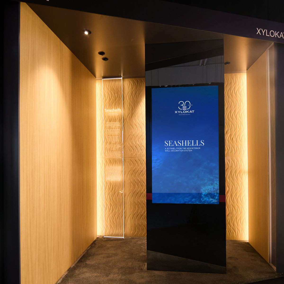 Exhibition corner with warm wooden walls, a textured Seashells wall section and a tall digital screen displaying the Seashells graphic.